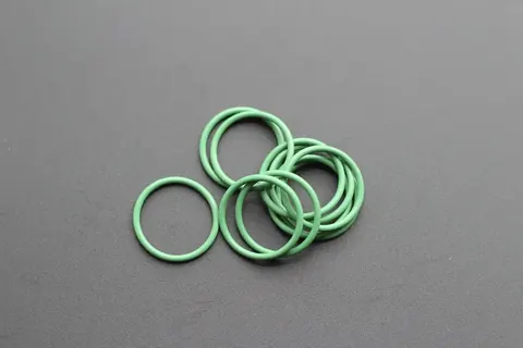 Four green FFKM O-rings of two diameters on a grey background