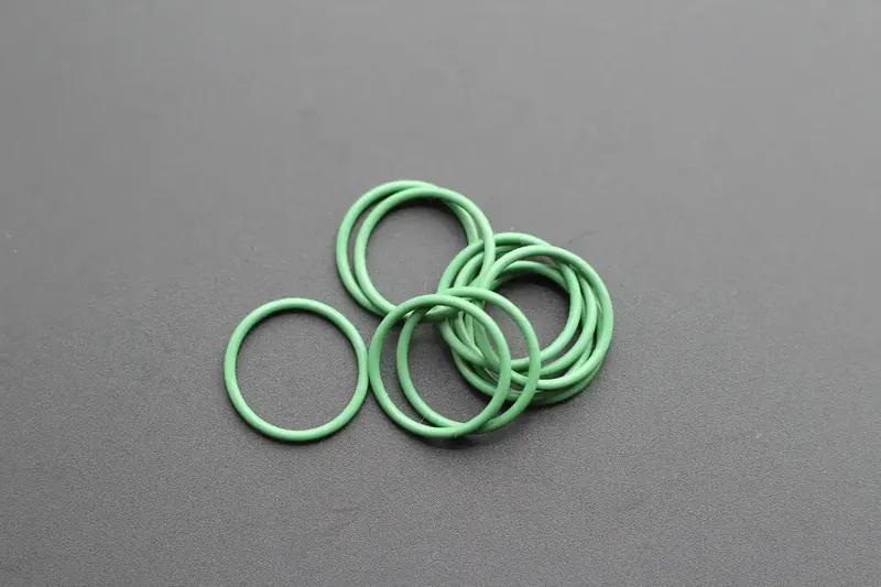 Green perfluoroelastomer O-rings arranged on a grey studio background
