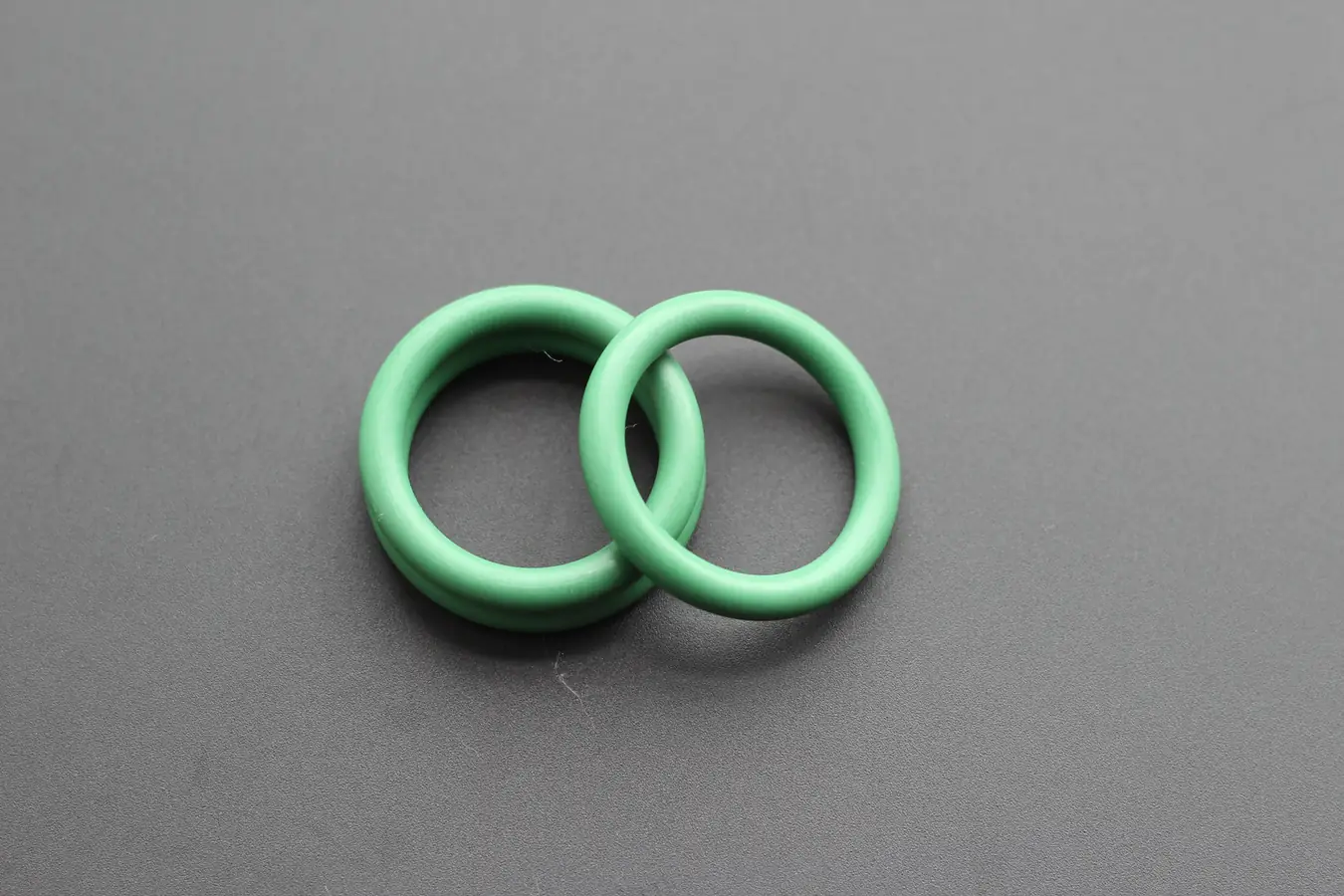 Two green perfluoroelastomer O-rings resting on a grey background