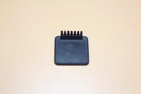 Small black moulded plastic component with a row of fine parallel teeth